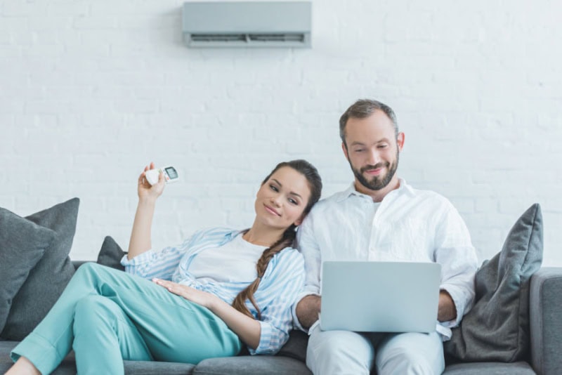 couple sitting on their couch using a remote controller to adjust their ductless system.