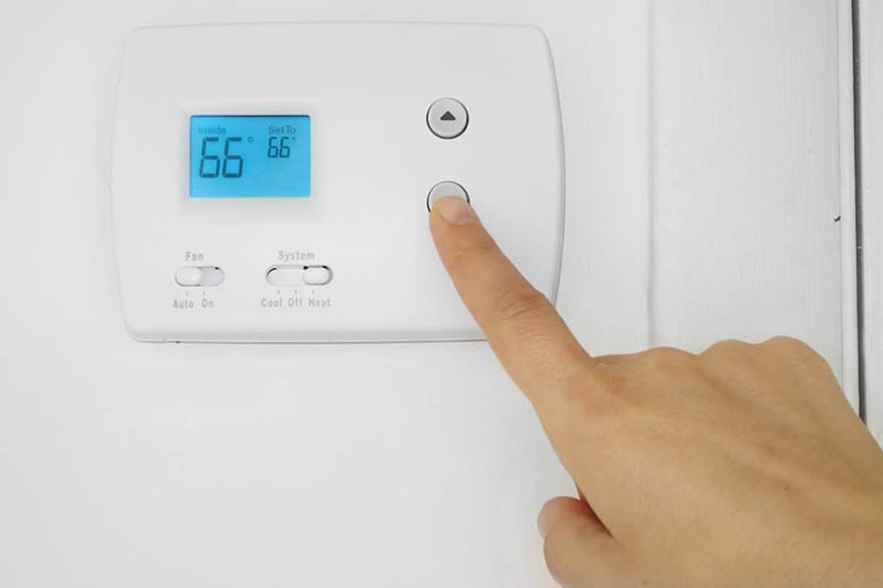 5 Reasons Why Regular HVAC Maintenance is Essential for Deschutes County Homeowners. Image is a photograph of a person's hand adjusting a wall mounted thermostat temperature.
