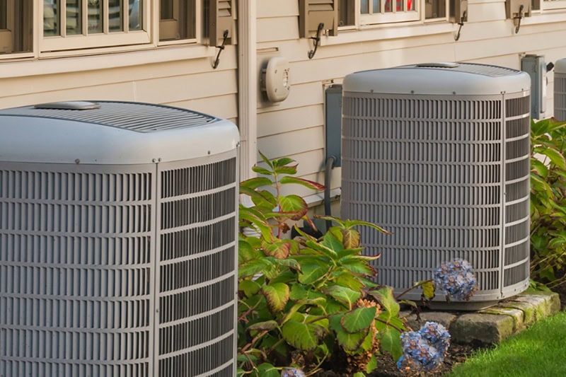 Spring AC Maintenance Tips. Photos of two air conditioning units installed outside of a home.